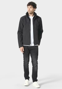 Czarna kurtka na zamek z kapturem, charakteryzująca się eleganckim fasonem, teksturowanym materiałem i kontrastującymi szwami, w połączeniu z czarnymi dżinsami i białymi trampkami.