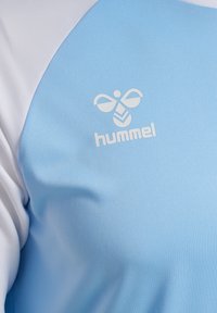 Lyseblå sportstrøje med hvide ærmer og hvidt logo. Glat tekstur med et moderne design. Ideel til atletisk brug.