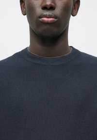 Marineblå strikket sweater med et struktureret mønster, rund halsudskæring og ribbede manchetter. Stoffet ser blødt ud med en subtil glans.