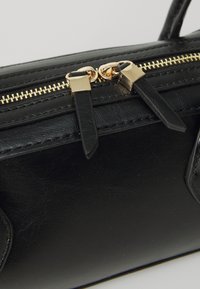 Schwarze Kunstleder-Handtasche mit goldfarbener Reißverschluss, doppelten Ziehlaschen und gesteppten Details auf der Oberfläche.