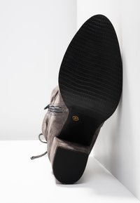 Bottine en daim gris avec semelle en caoutchouc noire texturée, design à lacets et détail de fermeture éclair latérale. Étiquette de taille visible sur le talon.