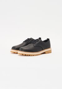 Black leather shoes with a rounded toe, stitched accents, and a beige rubber sole featuring a rugged tread pattern.