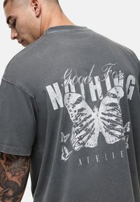 Grijs oversized t-shirt met een grote witte vlindergrafiek met skeletdetails en de tekst "Good For NOTHING ATELIER" op de achterkant.