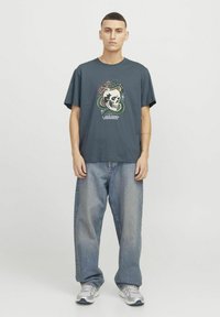 Mørkegrå bomulds t-shirt med et farverigt grafisk motiv af et kranium og en slange. Kombinationen er afslappede lyseblå denimjeans og sneakers.