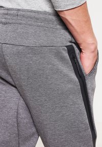 Gråa mjukisbyxor med ett texturerat tyg, med en sidoficka med svart dragkedja och en elastisk midjeresår för komfort.