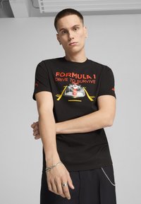 Juodas medvilnės marškinėliai su raudonu ir geltonu "Formula 1 Drive to Survive" grafinis motyvas, trumpomis rankovėmis ir Puma logotipu ant peties.