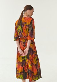 Bloemendress met oranje, groene en paarse patronen. Korte mouwen, tailleband, knielengte, gemaakt van lichtgewicht stof, met een luchtig ontwerp.