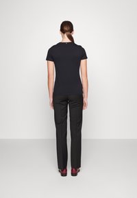 Top corto negro de manga corta, con forma ajustada y textura suave. Combinado con pantalones negros y zapatos burdeos, visto desde atrás.