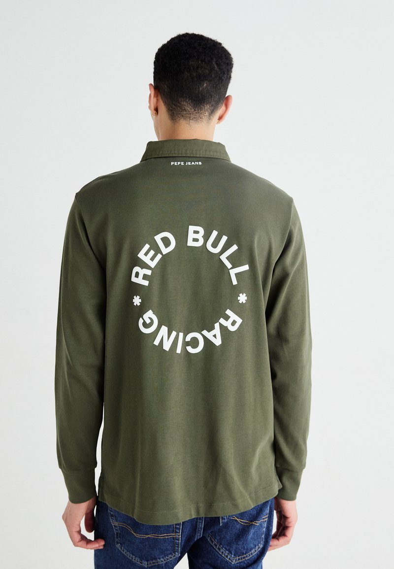 Olivno zelena polo majica z dolgimi rokavi in zaobljenim robom, na hrbtni strani pa se nahaja velika bela natisnjena značka, ki pravi "RED BULL RACING."