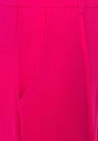 Pantalons en tissu rose vif montrant les détails de la poche avant, de la taille et des passants de ceinture en gros plan.