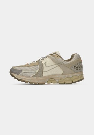 Sneaker sportivo beige e grigio con pannelli in rete e texture, lacci bianchi e suola imbottita.