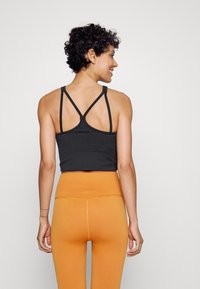 Top preto cropped com design de costas com tiras, combinado com leggings laranja de alta cintura e textura. Tecido suave, forma ajustada e cores contrastantes.