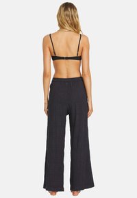 Pantalones negros de pierna ancha con una tela texturizada y una cinturilla elástica, vistos desde atrás. Con un diseño minimalista.
