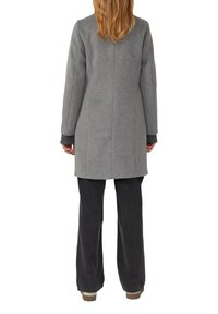 Grijze wollen jas, halflang, gestructureerd ontwerp, met geribbelde manchetten. Gepaard met donkere denim broek, met rechte snit en minimale details.
