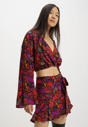 Completo due pezzi in stile uncinetto caratterizzato da un crop top a maniche lunghe con scollatura a V profonda e una mini gonna avvolgente. Vivace motivo floreale in rosso, viola e verde.