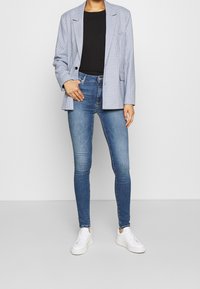 Světle modrý kostkovaný blazer, černý top, modré úzké džíny a bílé tenisky. Blazer má klopové límce a uvolněný střih.