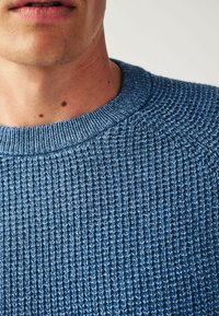 Gebreide trui met een textuurpatroon, gemaakt van blauwe garen. Beschikt over een ronde halslijn en geribde mouwen. Close-up afbeelding benadrukt de details van de stof.