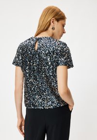 T-shirt met korte mouwen van een glinsterende stof in donkerblauw en zilver. Voorzien van een keyhole-detail aan de achterkant. Combinatie met een zwarte onderbroek.