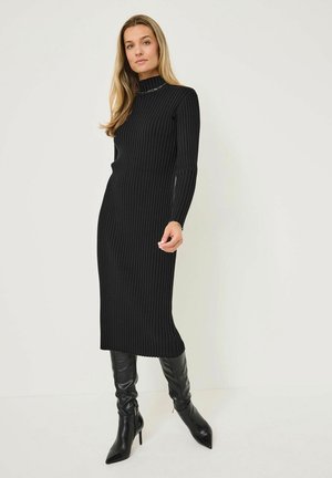 Abito a maglia nero a coste con maniche lunghe e collo alto, caratterizzato da una silhouette aderente e uno spacco laterale, abbinato a stivali neri con tacco alto.