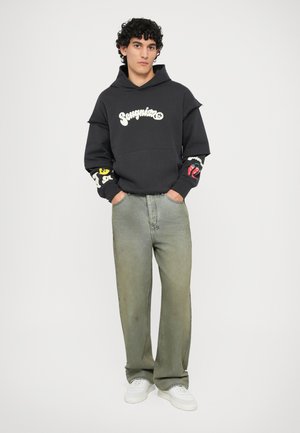 Sudadera negra con el logo "Songni", gráficos coloridos en las mangas; combinada con jeans verde claro de corte holgado y zapatillas blancas.
