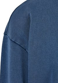 Tessuto a maglia blu con una texture fine, caratterizzato da un dettaglio sulla cucitura della spalla e una vestibilità rilassata. Il materiale appare leggero con una lucentezza sottile.