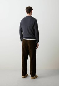 Maglione grigio scuro con maniche lunghe, abbinato a pantaloni in velluto a coste marroni con righe verticali. Calzature casual completano l'outfit.
