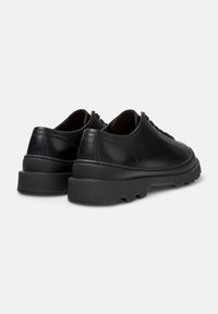 Scarpe nere in pelle con suola spessa, che mostrano la vista posteriore e la cucitura dettagliata lungo i bordi.