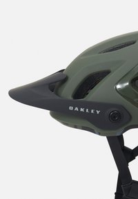 Capacete de ciclismo Oakley na cor verde oliva mate com detalhes em preto, forma aerodinâmica, aberturas de ventilação e sistema de retenção ajustável.