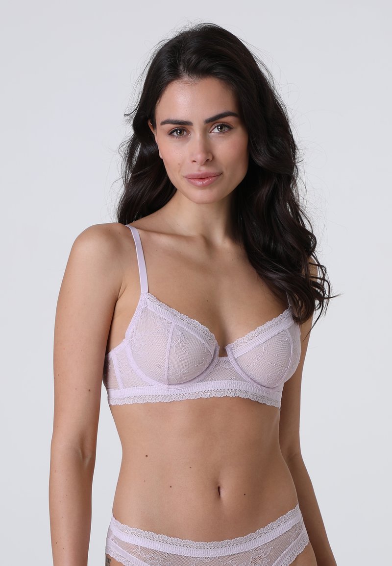 Reggiseno in pizzo lilla con coppe trasparenti, motivo floreale, spalline regolabili e bordi scallopati. Design delicato con texture morbida e un leggero luccichio.