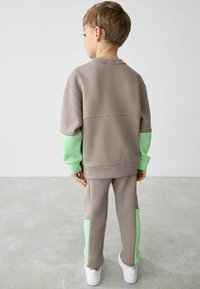Grau sweatshirt und Hosen Set mit mintgrünen Akzenten. Glatte Textur, lockere Passform und gerippte Bündchen. Weiße Schuhe vervollständigen das Outfit.