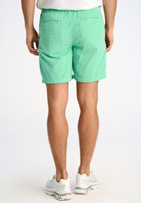 Pantaloni corti in corduroy verde con vita elastica, due tasche posteriori e taglio affusolato, abbinati a scarpe da ginnastica bianche.