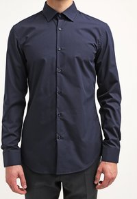 Camicia button-up a maniche lunghe di colore blu navy con una trama liscia, colletto classico e sei bottoni a contrasto sul davanti. Design slim-fit.