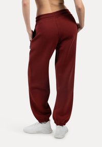 Bordeauxfarbene Sweatpants mit elastischem Bund und Bündchen, ausgestattet mit seitlichen Taschen und einem lässigen Schnitt, kombiniert mit weißen Sportschuhen.