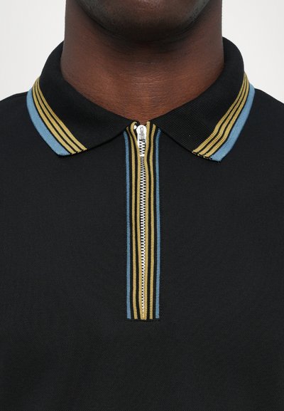 Polo negro con cremallera en el frente, con un cuello adornado con rayas azules y doradas, mostrando un tejido texturizado.