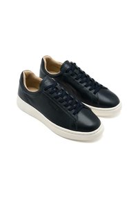 Zapatillas de cuero azul marino con suela de goma blanca. Tienen punta redonda, acentos perforados y cordones azul marino. Forro interior suave color tostado.