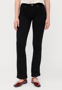 Svarta denimjeans med rak passform, med fem fickor och synlig sömnad. Bärs med röda, lackskinnskor utan klack.