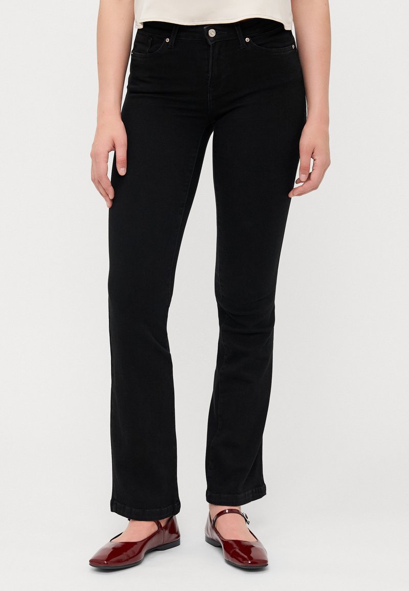 Svarta denimjeans med rak passform, med fem fickor och synlig sömnad. Bärs med röda, lackskinnskor utan klack.