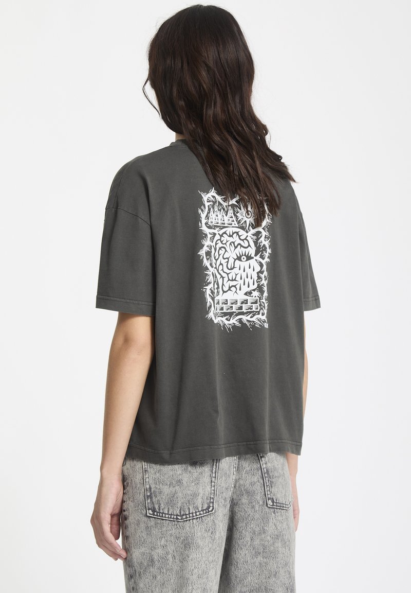 Camiseta de gran tamaño en gris oscuro con un diseño gráfico blanco en la parte posterior. El tejido parece suave, con un corte relajado y mangas cortas.