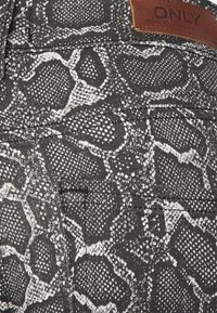 Tela negra con un patrón de piel de serpiente blanca, con una etiqueta de cuero etiquetada como "ONLY." Superficie texturizada con detalles de costura horizontal.
