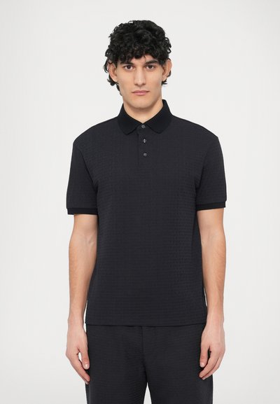 Polo noir avec un motif texturé, manches courtes et un col contrastant. Dispose de trois boutons au niveau de l'encolure.