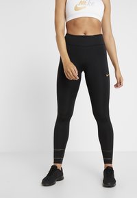 Leggings neri a vita alta con finitura liscia, dotati di un logo Nike dorato all'anca e di dettagli in cucitura dorata vicino alla caviglia.