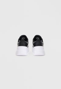 Črne športne copate z belimi podplati, ki imajo eleganten dizajn, teksturirano usnje na zgornjem delu, zanko na peti in minimalno blagovno znamko na jezikih.