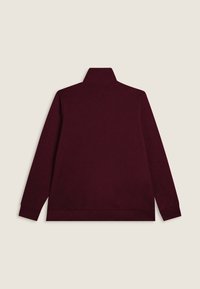 Pullover lungo a maniche lunghe di un borgogna scuro con colletto alto, mostrato da dietro su uno sfondo beige uniforme.