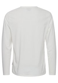 Hvid langærmet T-shirt lavet af blødt bomuld. Har en rund halsudskæring og lige kant med et mærke syet på den nederste side.