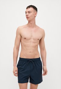 Pantaloni da bagno blu navy con righe verticali, vita elasticizzata, coulisse e texture liscia. Il modello si presenta con un'espressione neutra.