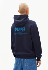 Navyblauwe hoodie met een capuchon en trekkoord, voorzien van een grote "DETOX" opdruk en tekst op de achterkant. Gemaakt van katoen, met geribbelde boorden en zoom.