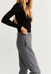 Zwart geribd longsleeve top gecombineerd met grijze, gestructureerde broek met zakken en een getailleerde pasvorm, weergegeven vanuit een zijaanzicht.