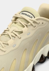 Gaiši beidži sporta apavi ar tīkla un zamša virsu, viļņainiem izgriezumiem, redzamām amortizācijas kabatām un teksturētu papēdi. "Air Max" zīmols uz mēles.