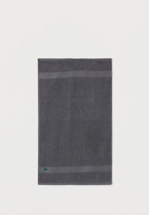 Σκοτεινό γκρι ορθογώνιο πετσέτα με υφή ρίγας κοντά στις άκρες και μικρό πράσινο λογότυπο κοντά στην κάτω αριστερή γωνία.
