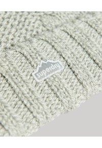 Jasnoszara, dziergana czapka beanie z prążkowanym wzorem i teksturowanym wykończeniem. Zawiera biały logo naszywkę z przodu.